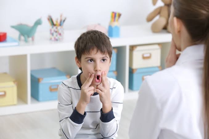 Niño practicando movimientos de boca frente a una terapeuta en una sala infantil
