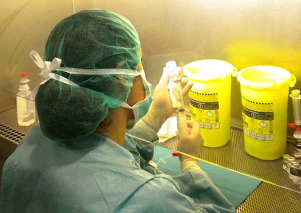 Profesional con gorro y mascarilla preparando un citostático en cabina de bioseguridad