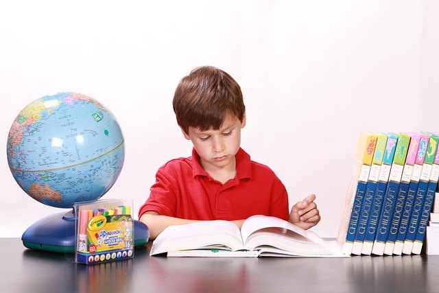 Niño de polera roja lee un libro grande junto a un globo terráqueo