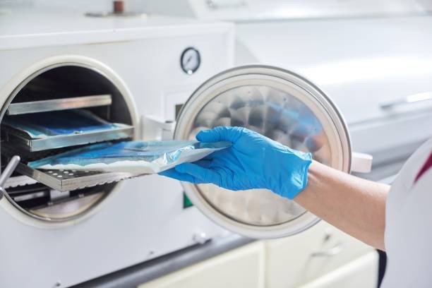 Mano con guante azul cargando material empaquetado en un autoclave