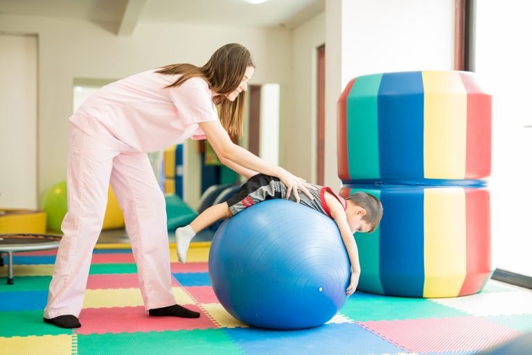 Terapeuta guía a un niño recostado sobre un balón terapéutico