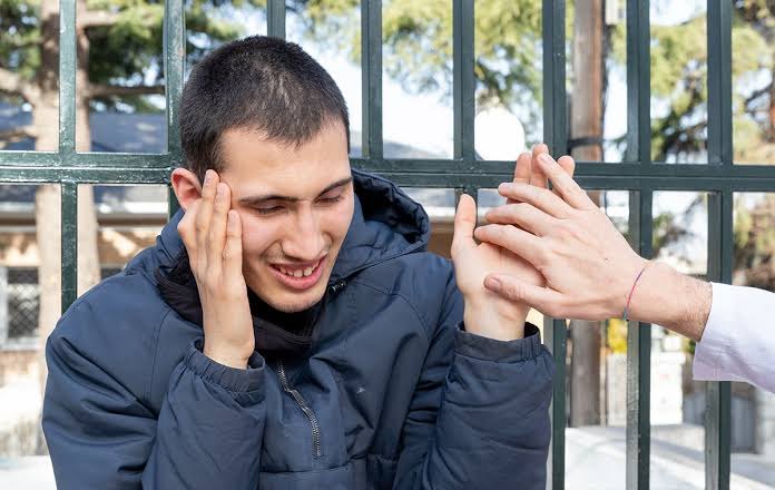 Joven se cubre las orejas con las manos mientras otra persona le ofrece apoyo