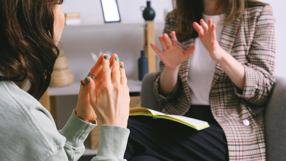 Psicóloga conversa con una paciente en una sesión, con un cuaderno abierto